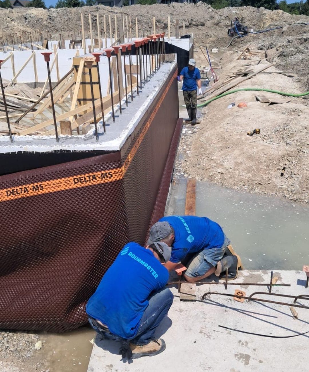 AquaMaster crew installing Delta-MS dimple membrane on a new foundation with rebar